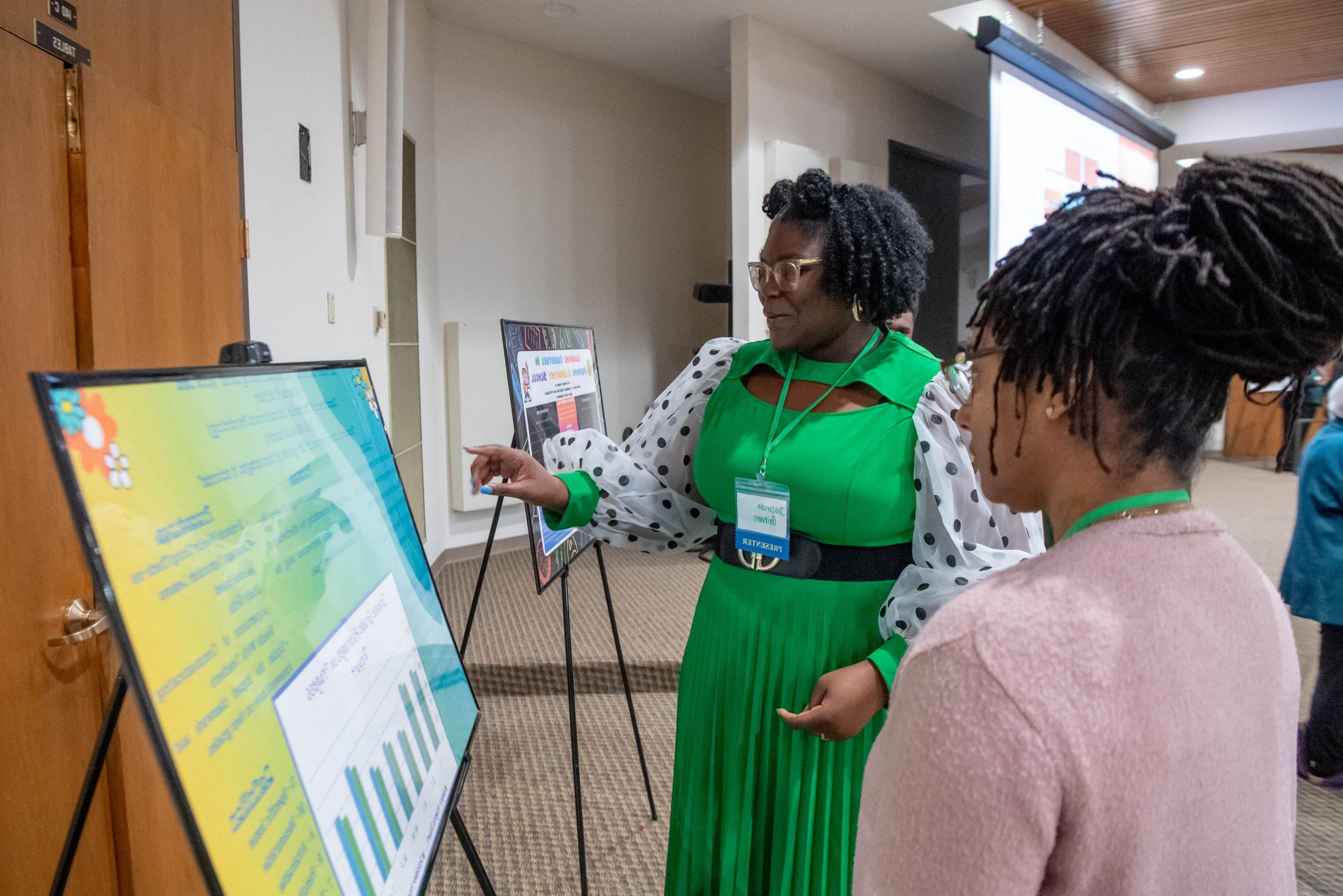 Student presenting research poster information to a person standing next to her.