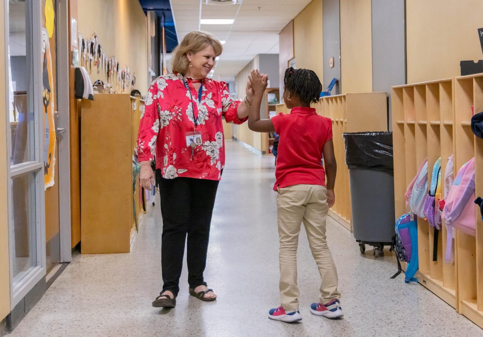 School administrator giving an elementary student a high-five in the hallway.